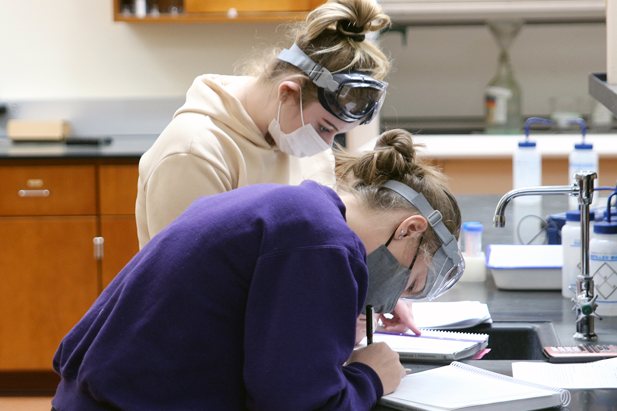 Two students in masks and goggles working in a lab