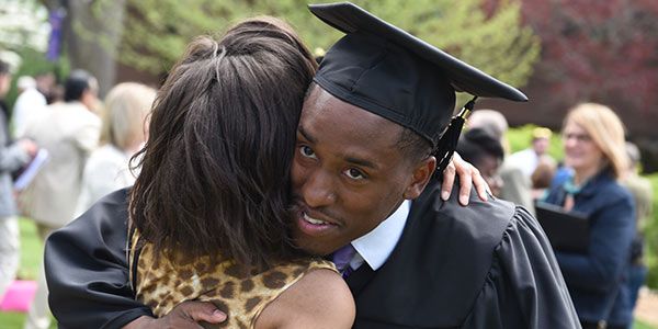 A student in a cap and gown hugging someone.