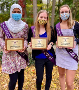 Three students outside holding plaques.