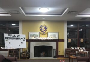 Kellogg Center living room with fireplace and shield emblem above mantel piece, decorated with photographs in remembrance of transgender people who were killed in 2023 and a larger sign that says Wall of Remembrance